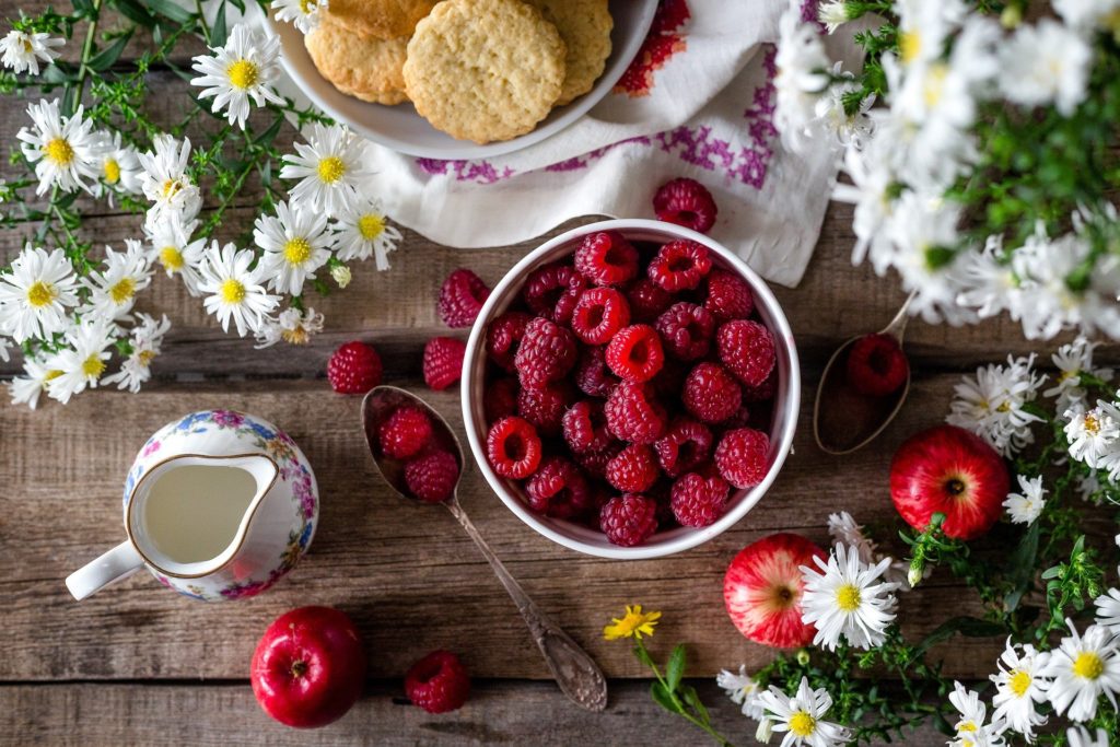 Raspberries in a bowl with white daisies scattered around it