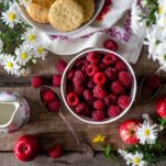 Raspberries in a bowl with white daisies scattered around it